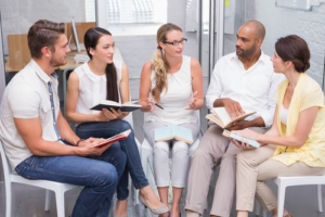 Men and Women sitting in a semi-circle with books in their hands
